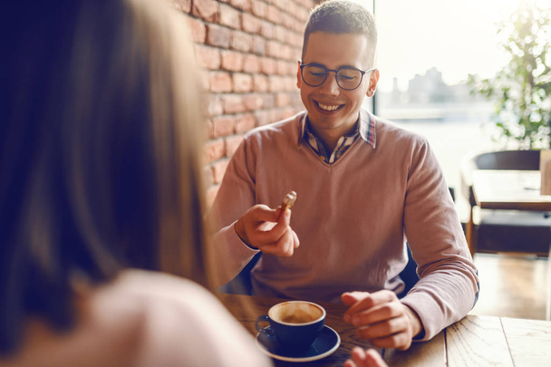 Κομψό Καυκάσιος ευτυχισμένο ζευγάρι κάθεται στο καφέ, πίνοντας καφέ και βλέπουν ο ένας τον άλλον. Σε φόντο τοίχο από τούβλα. - Φωτογραφία, εικόνα