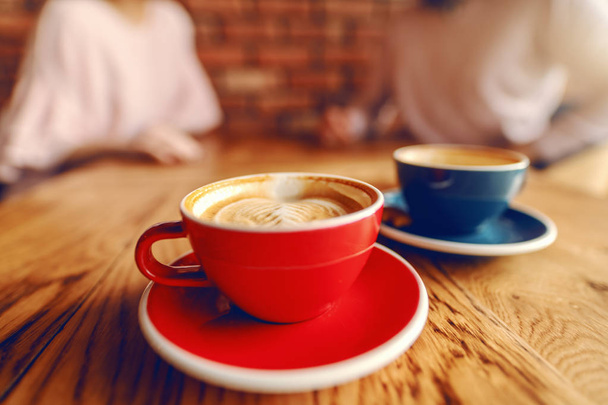 Close up of two cups of coffee on desk. In background blurred couple flirting. - Photo, Image