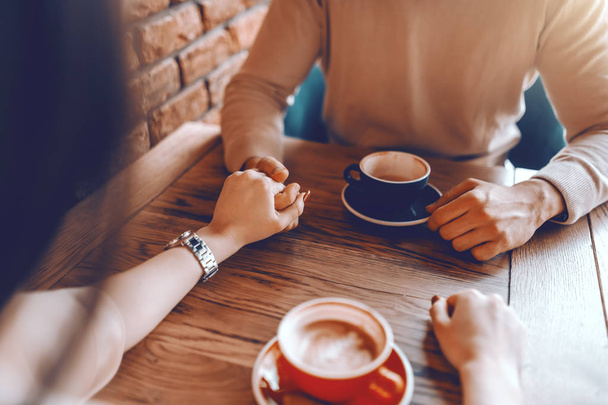 Caucasian Couple in love sitting in cafeteria, drinking coffee and holding hands. Cropped image. - Фото, изображение