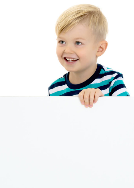 A little boy looks through an empty banner on which you can write any text. The concept of a happy childhood and advertising of childrens goods. Isolated on white background. - Fotografie, Obrázek