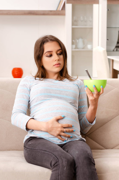 Fiatal terhes nő ül a kanapén, otthon  - Fotó, kép