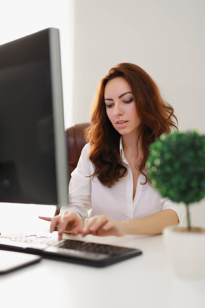 Beautiful businesswoman working in white office looking at computer monitor - Foto, Imagem