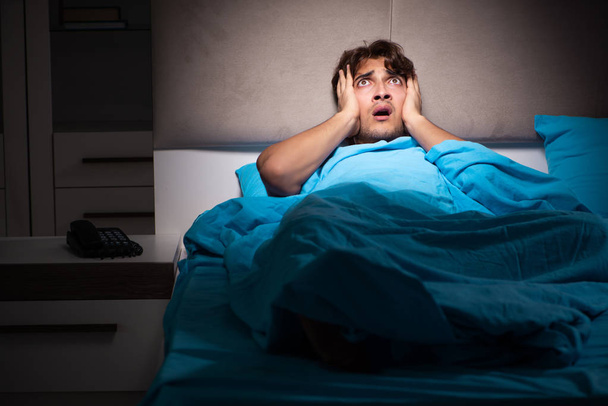 Young man scared in his bed having nightmares - 写真・画像