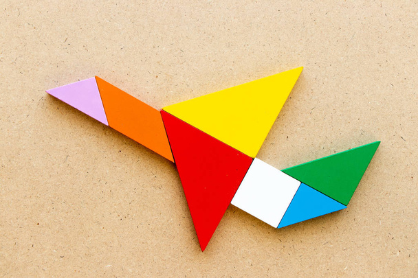 Color tangram in flying airplane shape on wood background - Photo, Image