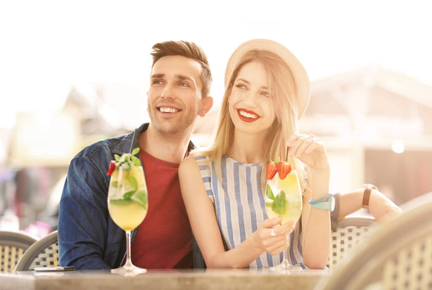 Young beautiful couple with glasses of refreshing drink in open-air cafe on sunny day  - Foto, immagini