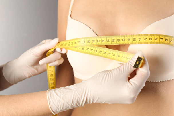 Doctor measuring size of patient's breast on gray background, closeup. Cosmetic surgery - Valokuva, kuva