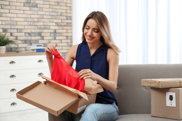 Young woman opening parcel on sofa in living room - Photo, Image