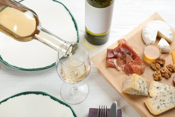 Pouring white wine into glass on table with delicious food - Foto, immagini