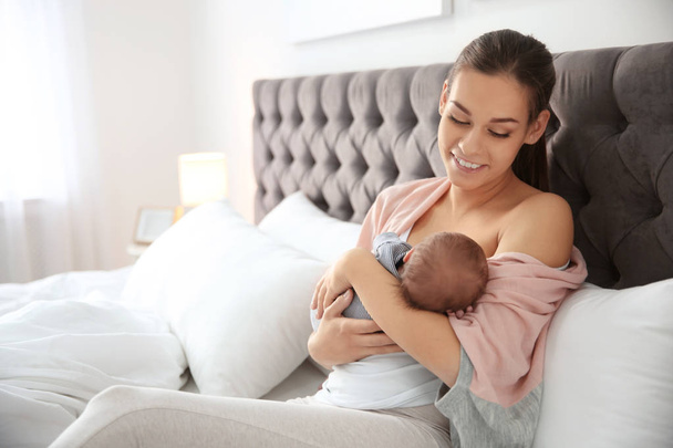Young woman breastfeeding her baby in bedroom - 写真・画像