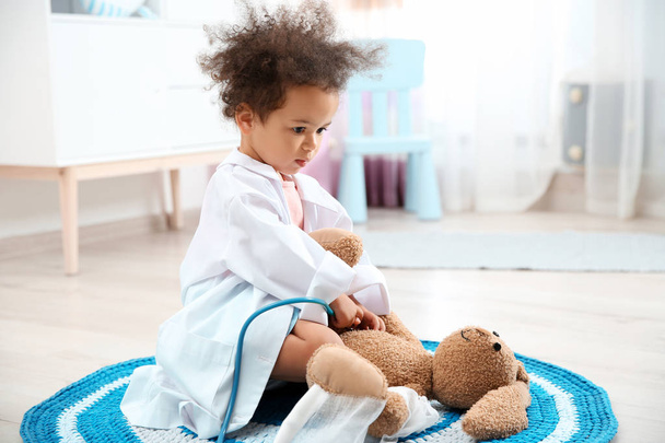 Cute African American child imagining herself as doctor while playing with stethoscope and toy bunny at home - Foto, Bild