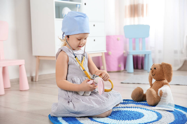 Cute child imagining herself as doctor while playing with stethoscope and toy bunny at home - Fotoğraf, Görsel