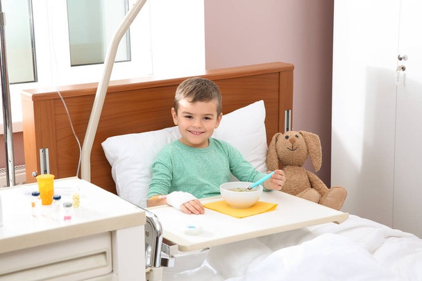 Little child with intravenous drip eating soup in hospital bed - Φωτογραφία, εικόνα
