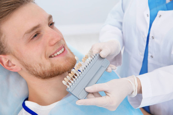 Стоматолог підбирає колір зубів пацієнта з палітрою в клініці
 - Фото, зображення