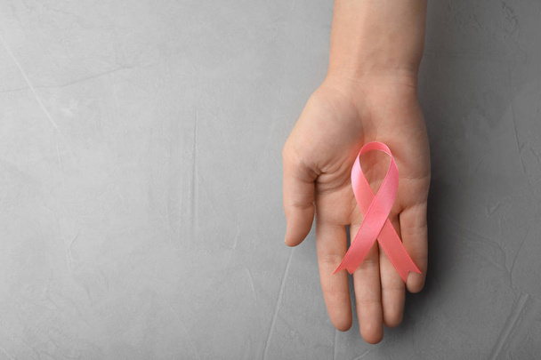 Woman holding pink ribbon on grey background, top view with space for text. Breast cancer awareness concept - Fotografie, Obrázek