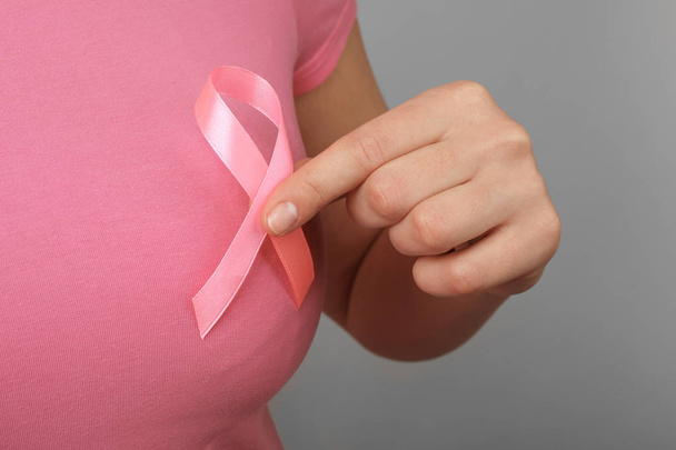 Woman holding pink ribbon on grey background, closeup. Breast cancer awareness - Foto, afbeelding
