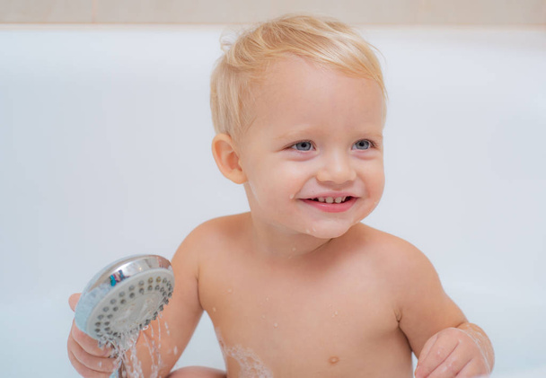 Smiling kid in bathroom with toy duck. Smiling baby boy bathing under a shower at home. Little child bathing in soapsuds. - Fotó, kép