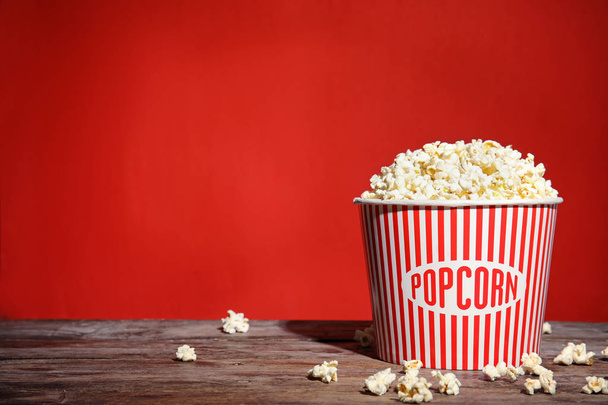 Bucket of tasty popcorn on table against red background, space for text. Watching cinema - Foto, afbeelding