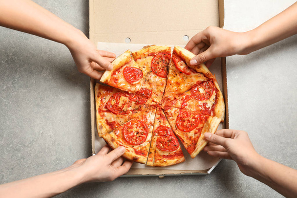 Young people taking slices of hot cheese pizza from cardboard box at table, top view. Food delivery service - Фото, зображення