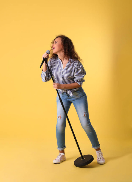 Curly African-American woman singing in microphone on color background - Fotoğraf, Görsel