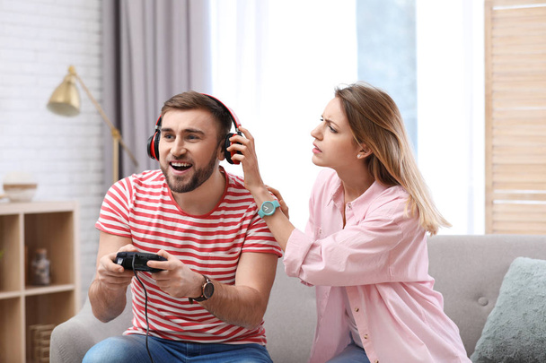 Joven jugando videojuego en casa mientras su novia se enoja con él
 - Foto, Imagen