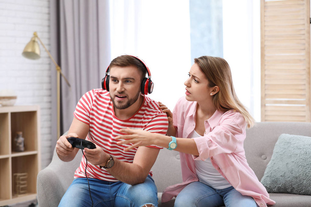Young man playing video game at home while his girlfriend angry with him - Foto, immagini