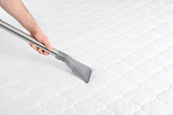 Man disinfecting mattress with vacuum cleaner, closeup. Space for text - Photo, image