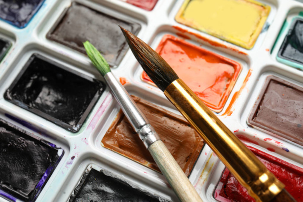 Plastic palette with colorful paints and brushes, closeup - Zdjęcie, obraz