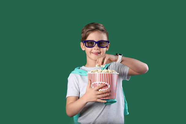 Cute boy in 3D glasses with popcorn bucket on color background - Foto, imagen