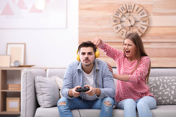 Young woman trying to draw attention of her man playing video games at home - Foto, Imagem