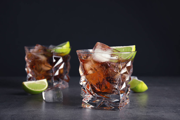 Glass of refreshing drink with ice cubes and lime on table against dark background - Foto, afbeelding