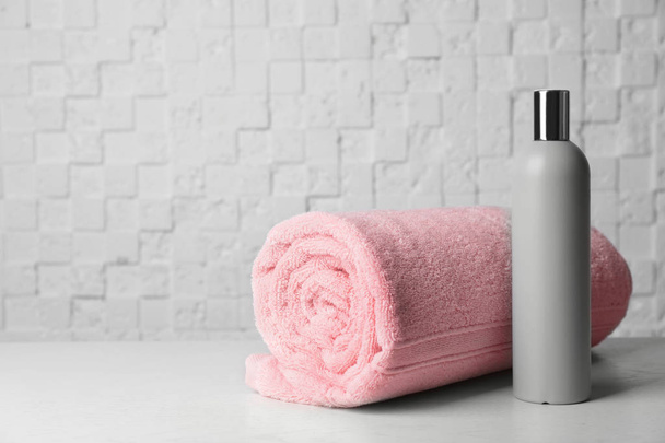 Bottle with shampoo and rolled bath towel on table, space for text - Foto, Bild