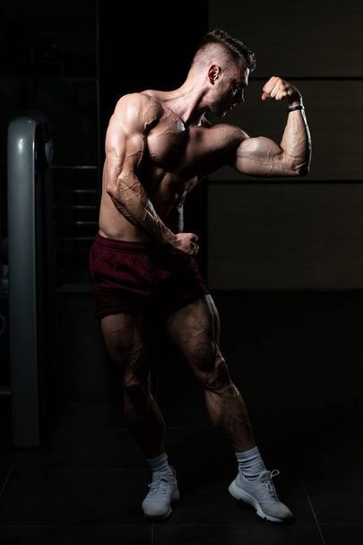 Young Man Standing Strong In The Gym And Flexing Muscles - Muscular Athletic Bodybuilder Fitness Model Posing After Exercises - Zdjęcie, obraz
