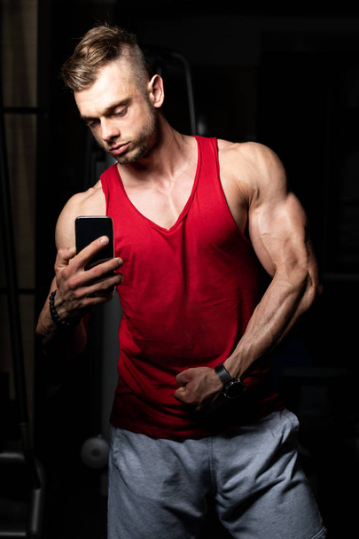 Young Fit Adult Man Taking A Selfie With Mobile Phone In Fitness Center - Gym In The Background - Foto, Bild