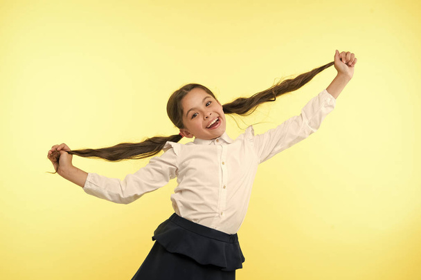 Happy girl show long brunette hair on yellow background. Little child smile with new hairstyle. Hairdresser salon services. Proud of her beautiful hair. Beauty salon. Stylish and cute - Fotoğraf, Görsel