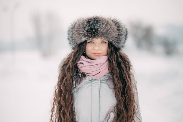 portrait of beautiful smiling female in luxurious fur head cloth outdoor in winter long hair - Photo, Image