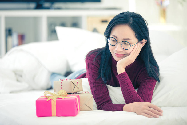 Riposo femminile sul letto e scatola regalo alla ricerca con volto sorriso
. - Foto, immagini
