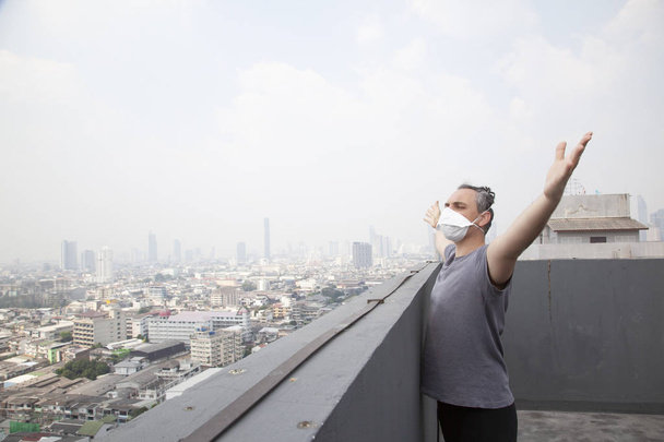ενήλικος άνθρωπος στην προστατευτική μάσκα των χειρών στη στέγη με αστικό τοπίο - Φωτογραφία, εικόνα
