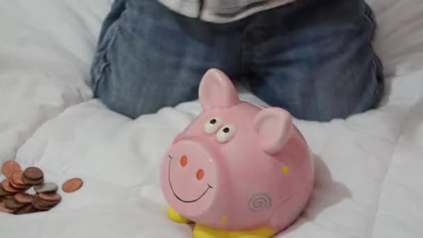 cute two years old baby boy playing with piggy bank and putting coins inside - Footage, Video