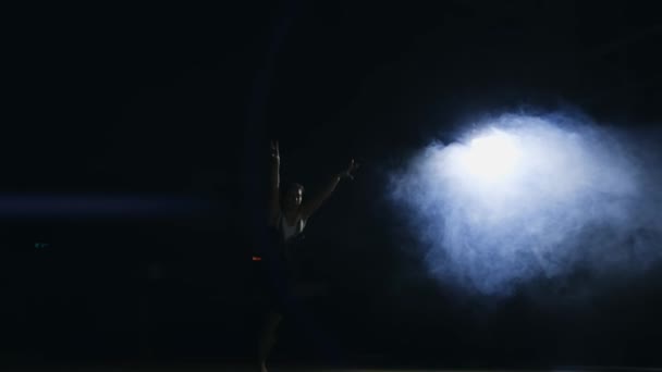 Het meisje loopt omhoog voert draaiingen en draait in de sluiting in slow-motion in de rook in de sportschool op het tapijt van de gymnastiek - Video