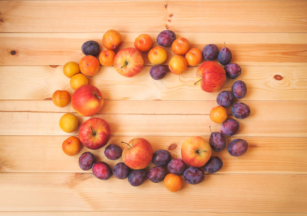Frame made of ripe apples and fresh purple and yellow plums on wooden background. Top view, copy space. - Photo, Image