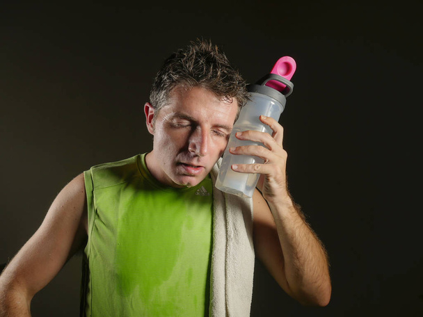 young sweaty tired and exhausted sport man with water bottle cooling off after hard fitness workout at gym club isolated on black background in healthy lifestyle and training sacrifice  - Foto, immagini