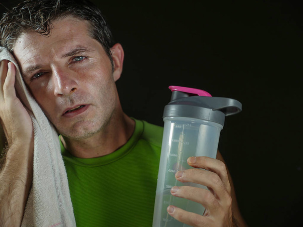young sweaty tired and exhausted sport man with water bottle cooling off after hard fitness workout at gym club isolated on black background in healthy lifestyle and training sacrifice  - Foto, immagini