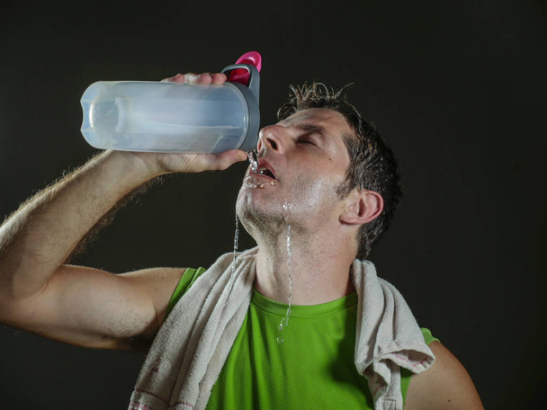 young sweaty attractive and fit sport man drinking water holding bottle cooling off after hard fitness workout at gym club isolated on black background in healthy lifestyle and training - Foto, Imagem