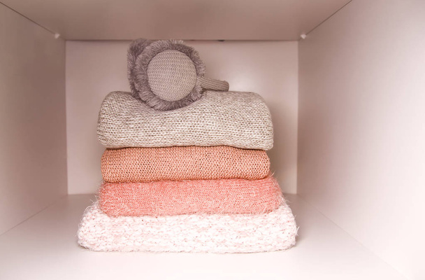 White shelf of the home wardrobe with colorful sweaters, jumpers and warm headphones. Small space organization, minimalism concept. - Photo, Image