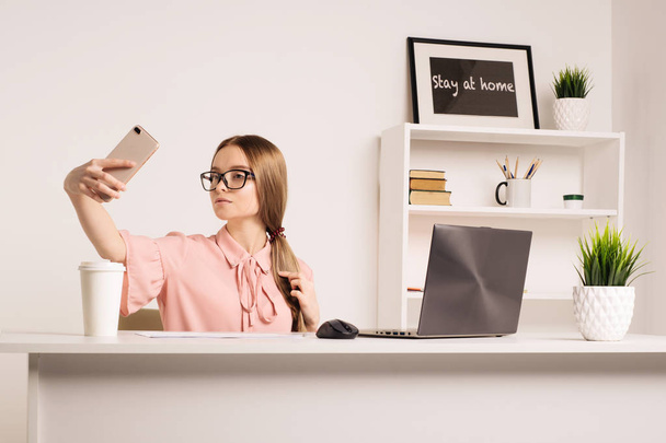 Portret van een speelse jonge meisje dat neemt selfie met mobiele telefoon zittend met laptop - afbeelding - Foto, afbeelding