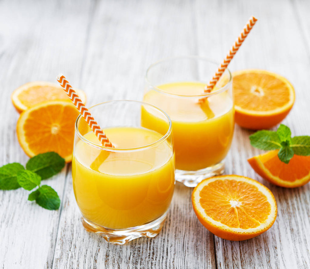 Glazen SAP en oranje vruchten op een houten tafel - Foto, afbeelding