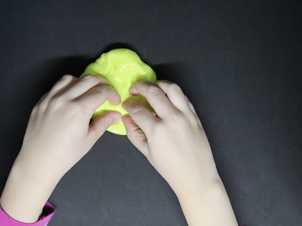 Dziewczyna bawiąca się żółtym śluzem w dłoniach. - Zdjęcie, obraz