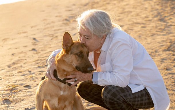 Portrait of beautiful widow older woman and german shepard dog enjoying its companion and love on beach in Benefits of animals Active Retirement lifestyle and Dog friendly tourism in afternoon light. - Фото, зображення
