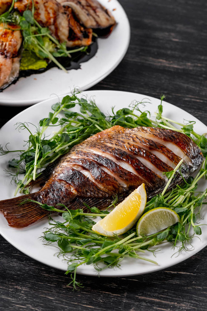 Whole baked fish served on green salad pillow with lemon slices  - Foto, Bild