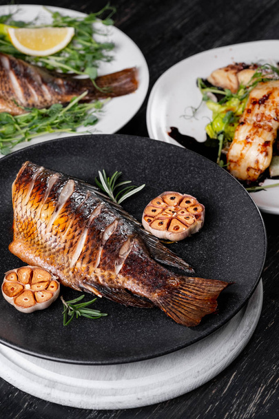 Fresh whole baked fish with rosemary twigs served on plate with baked garlic - Foto, Bild